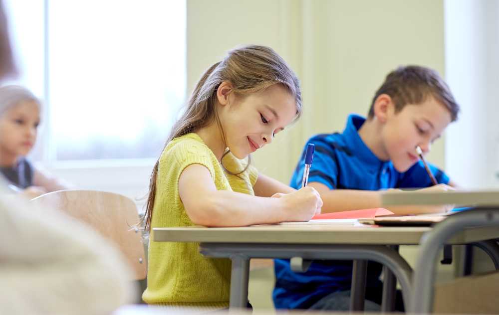 Group of school kids with pens and notebooks writing test in classroom