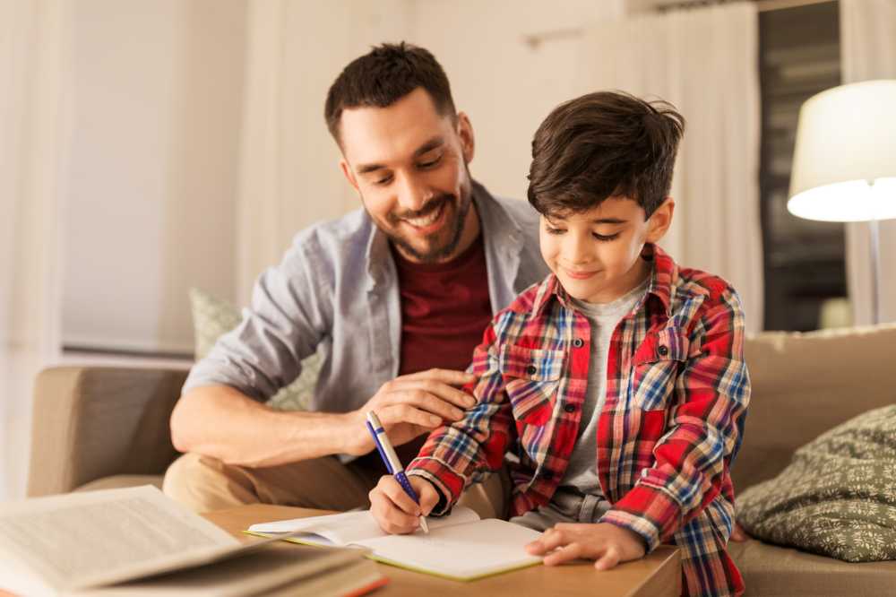 Happy father and son with book writing to notebook at home